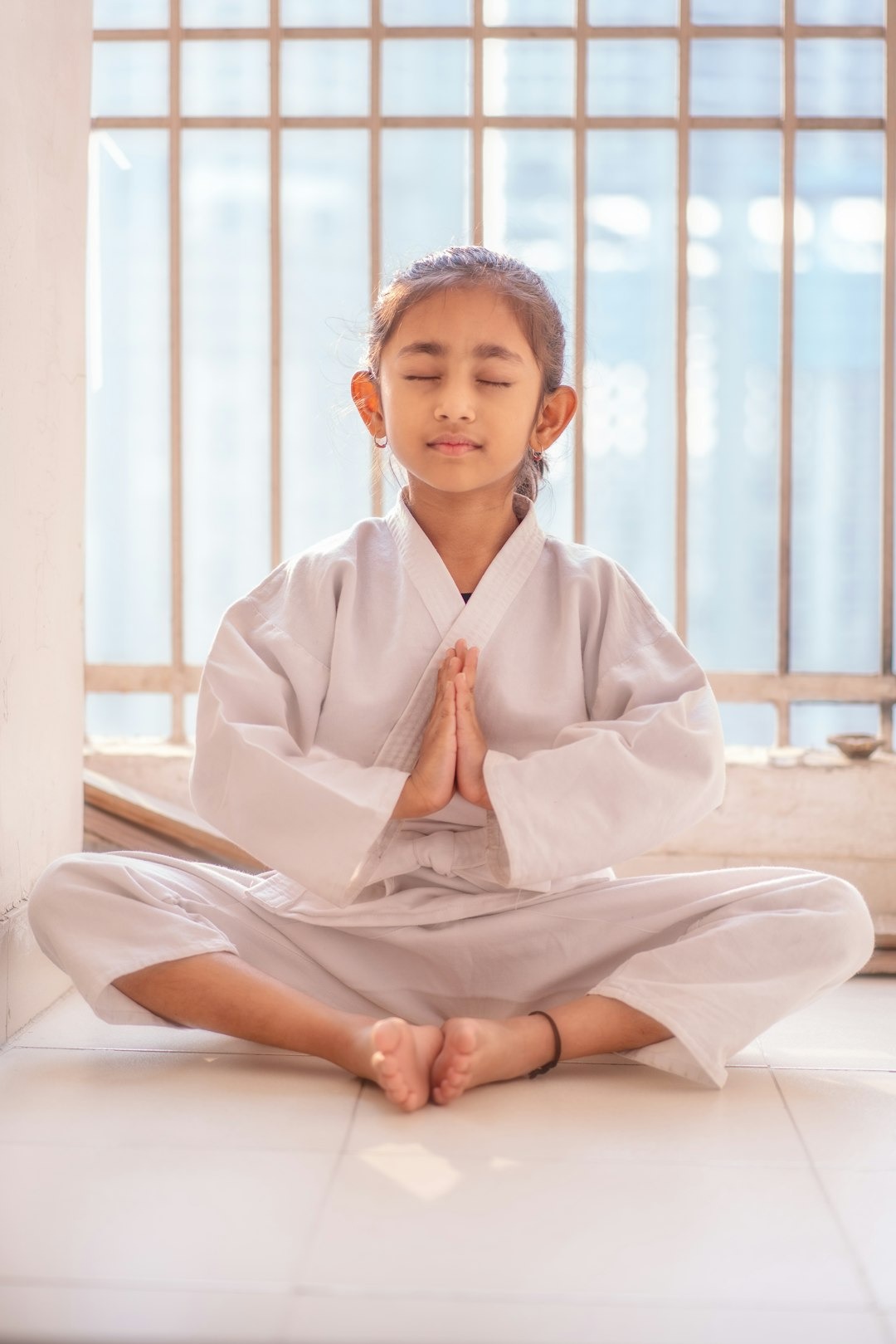 Girl in a martial arts uniform meditates with hands together.