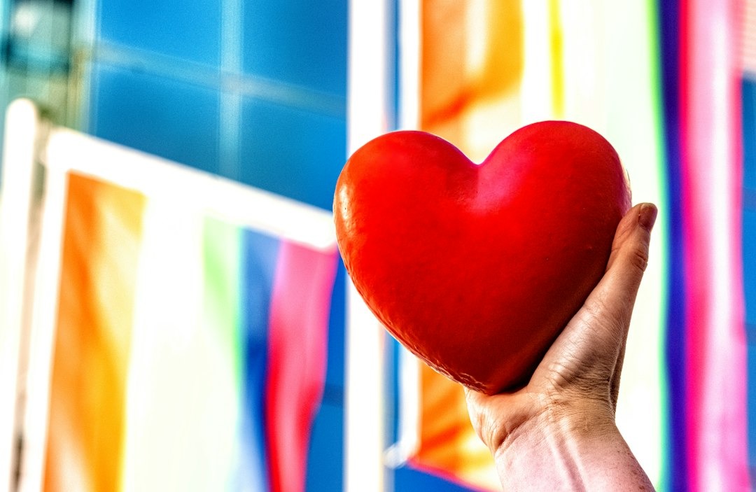 A hand holds a glossy red heart ornament.