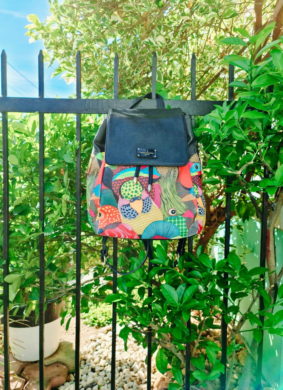 Colorful patterned backpack hanging on a black metal fence.